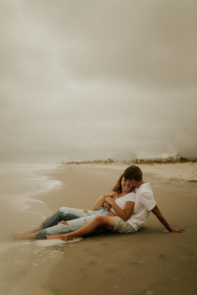 A north carolina couple sitting on the ocean isle beach during their engagement photoshoot