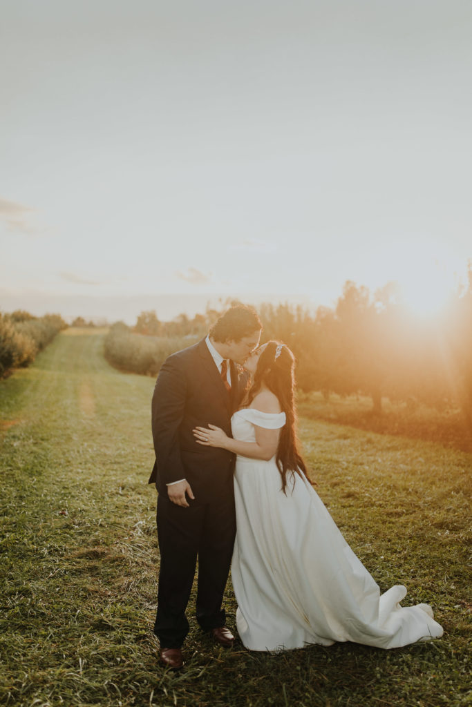 A newly wedded couple kissing with the sunset right after their wedding ceremony in an apple orchard