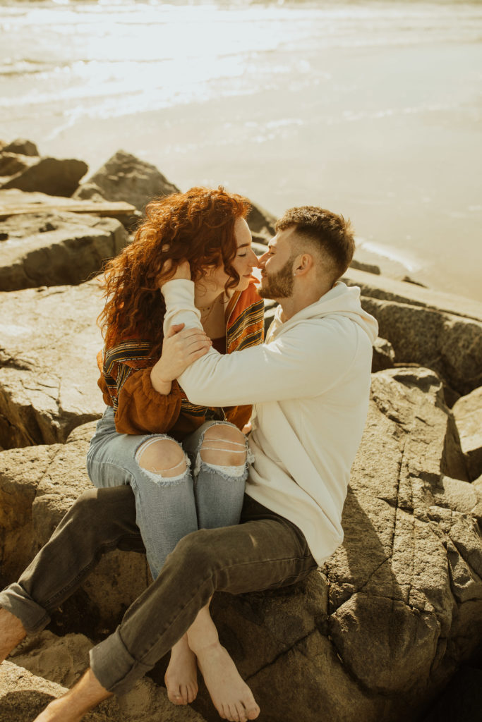 A couples photoshoot sitting on rocks at the beach in city new jersey 