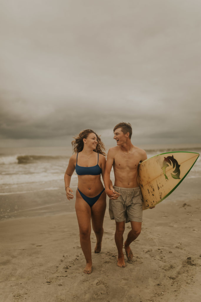 A north carolina couple posing with their surfboard on the ocean isle beach during their engagement photoshoot